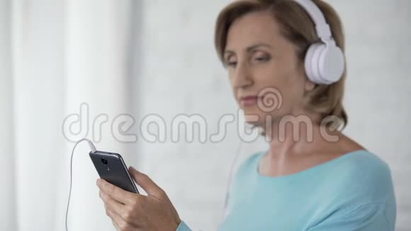 戴耳机的老年女性手机滚动屏幕选择歌曲视频的预览图