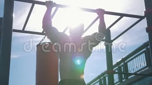 在阳光明媚的一天肌肉发达的人在户外的水平杆上被拉起来的后视图视频的预览图