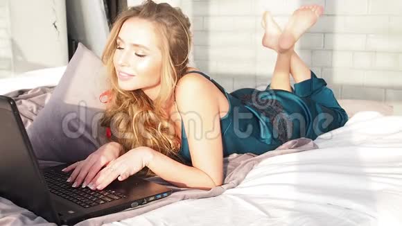 漂亮的少女笑着用笔记本电脑分享社交媒体躺在家里的床上视频的预览图