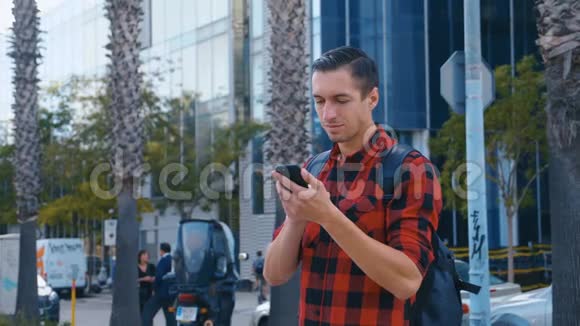 穿格子衬衫和背包看相机的英俊年轻人的肖像大玻璃城市建筑视频的预览图