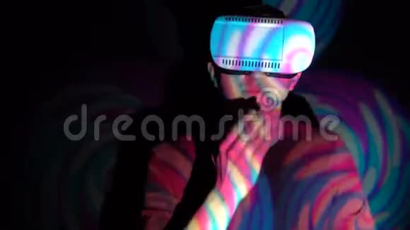 戴着虚拟现实眼镜的年轻人在明亮的聚光灯背景下进行空中亲吻视频的预览图