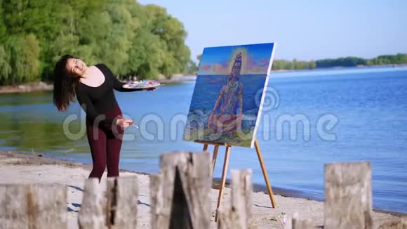 夏天河边海滩上日出时一位穿着紧身西装的漂亮女艺术家画了一幅画她的头发视频的预览图
