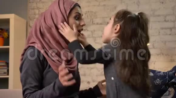 一个小女孩用头巾亲吻她的母亲坐在沙发上家庭家庭家庭舒适的概念母亲和女儿50视频的预览图