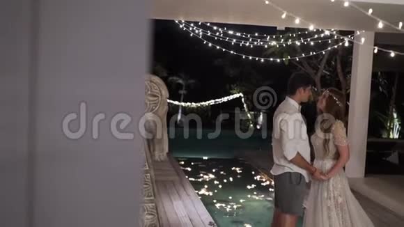 新娘和新郎晚上在热带别墅拥抱和亲吻背景灯视频的预览图