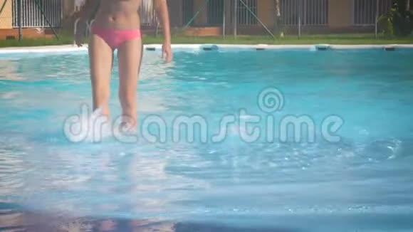 穿着粉红色泳衣的年轻苗条晒黑的女人站在室外游泳池里享受水流视频的预览图