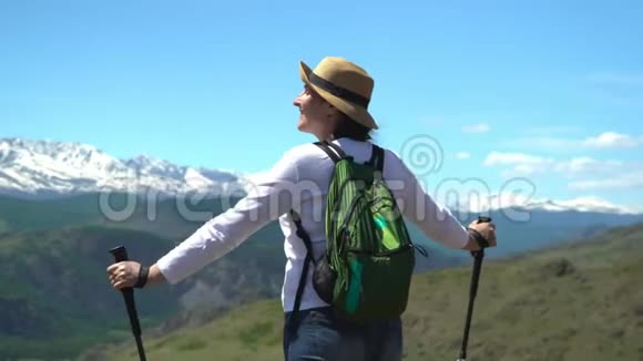 那个带着绿色背包的旅行者的女人在山上花钱看着白色的山脉视频的预览图