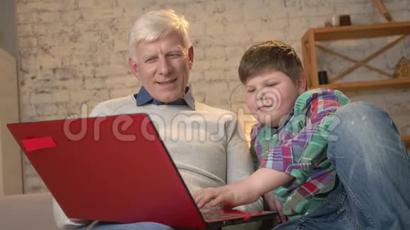 年轻的胖男孩教爷爷如何使用笔记本电脑不同的世代家庭舒适家庭闲适温馨视频的预览图