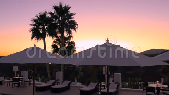 美丽的日落在豪华酒店与棕榈白色雨伞和躺椅提供水疗度假胜地的晚间放松视频的预览图