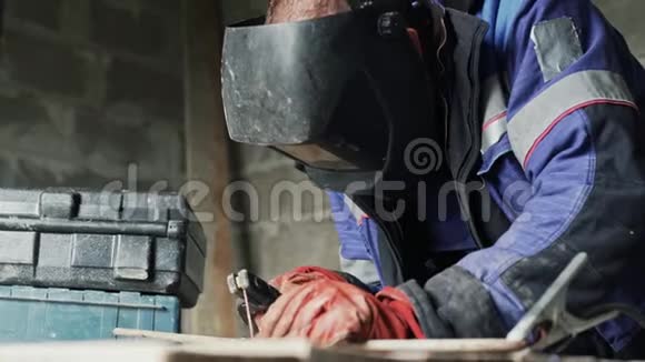 侧视焊机在焊接面罩焊接两个金属零件穿工作服的工人在室内工作视频的预览图