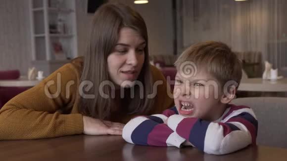 妈妈安慰小儿子她坐在咖啡馆里的一张桌子儿子视频的预览图