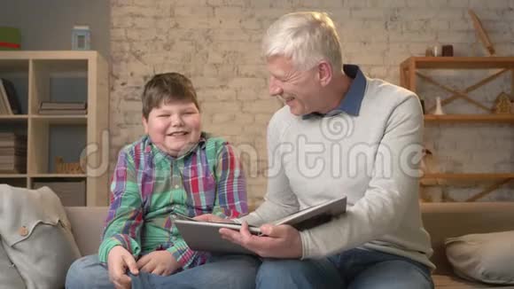 老人正在教一个年轻的胖子祖父和孙子正在读一本有趣的书微笑着幸福的家庭视频的预览图