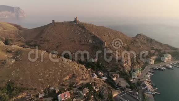 空中无人驾驶飞机飞向一座古老的堡垒俯瞰着群山和大海中的日落视频的预览图