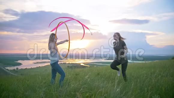 两个年轻的女人在山上锻炼女孩在日落时跳过山上的箍视频的预览图