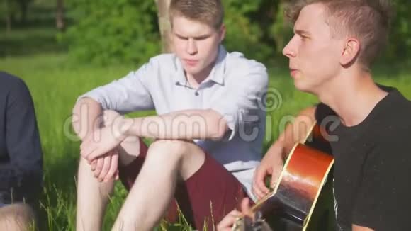 年轻的朋友们坐在草地上用吉他唱歌视频的预览图
