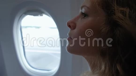 优雅的成年女人坐在飞机里望着蓝天上的舷窗在手机里发短信视频的预览图