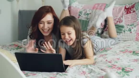 快乐可爱的女儿和年轻的妈妈在网上和爸爸或奶奶一起用躺着的笔记本电脑打视频电话视频的预览图