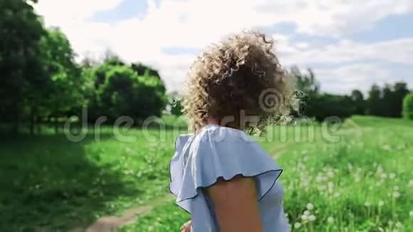 在阳光明媚的夏日一个迷人的女孩在风中摇着头发对着绿色的花园微笑视频的预览图