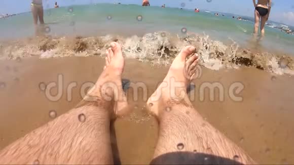 游客坐在海滩上因为海浪而把她的脚弄湿了视频的预览图