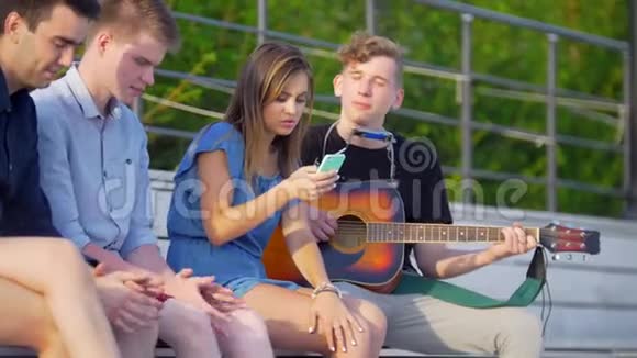 年轻的朋友们嬉皮士们在公园里休息用吉他听歌视频的预览图