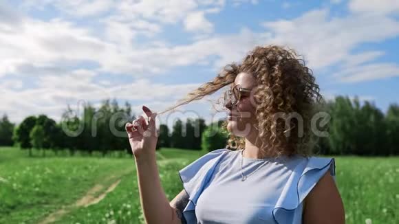 在阳光明媚的夏日一个迷人的女孩在风中摇着头发对着绿色的花园微笑视频的预览图