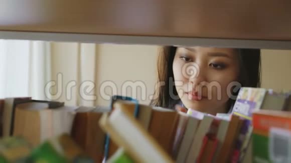 美丽的亚洲有思想的学生女孩在大图书馆的书架上寻找必要的书其中一个打开视频的预览图
