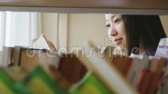 漂亮的亚洲学生女孩站在书架旁边大学图书馆里拿着书翻页视频的预览图