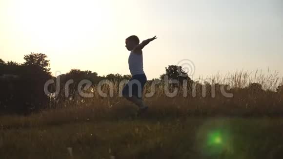 在阳光明媚的日子里一个像飞机一样举起双手在草地上奔跑的小男孩小孩在草坪上慢跑视频的预览图