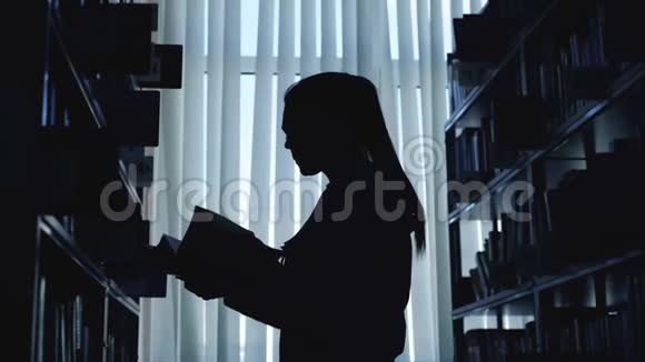 年轻的学生女孩站在大图书馆的书架上靠窗拿着书翻过来视频的预览图