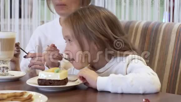 侧景迷人的女孩坐在美丽的年轻母亲旁边吃甜点视频的预览图