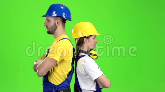 两个建筑工人背靠背站着手指伸直绿色屏幕慢动作视频的预览图