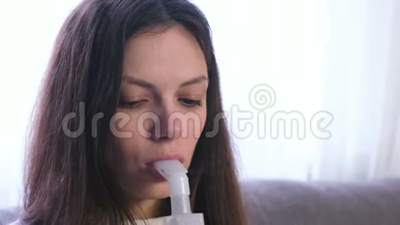 使用雾化器和吸入器进行治疗年轻女性坐在沙发上用吸入器喷嘴吸入喉咙视频的预览图