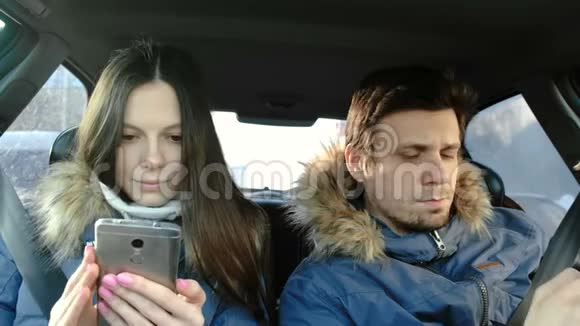 女人用手机给男人看东西他们穿着蓝色羽绒服坐在车里前景视频的预览图
