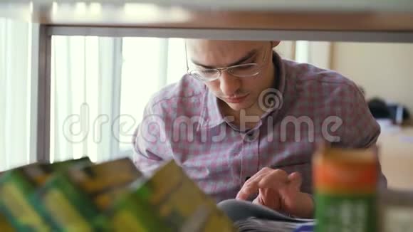 年轻英俊的白种人男学生戴着眼镜站在书架前拿着翻页的书视频的预览图