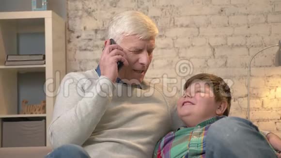 祖父和孙子坐在沙发上老人手里拿着一部智能手机在电话里交谈给出视频的预览图