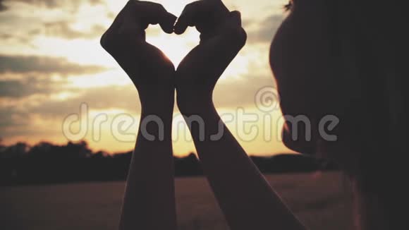 日落背景下一个年轻女子手中的心脏符号剪影视频的预览图