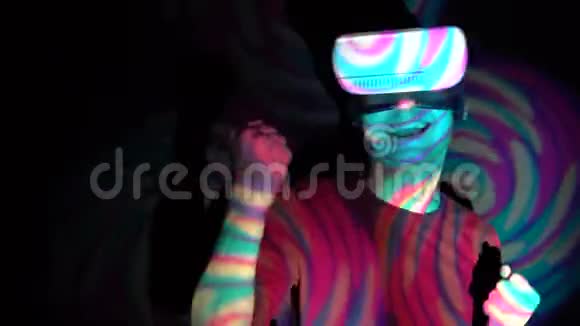 虚拟现实耳机中的年轻人在明亮的聚光灯背景下做赢家手势视频的预览图