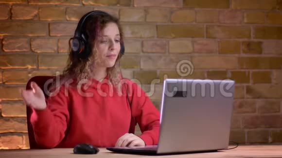 年轻女性博客作者的肖像红色帽衫记录视频使用笔记本电脑在布里肯墙背景视频的预览图