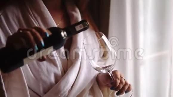 年轻女子把一瓶红酒倒进玻璃杯里住在阳台窗户附近的女孩穿着白色酒店视频的预览图