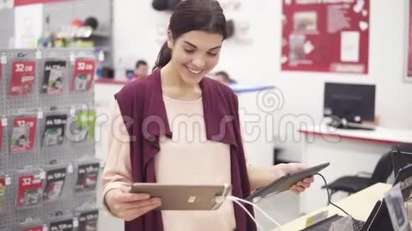 年轻美丽的黑发女孩微笑着在两片灰色和金色之间选择贴在货架上视频的预览图