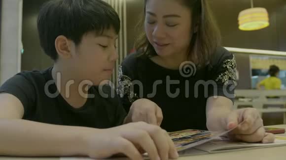 4K慢动作的亚洲可爱男孩与母亲阅读菜单书和点快乐的脸视频的预览图
