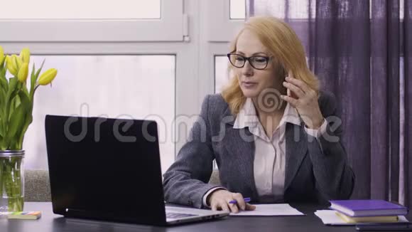 工作中使用笔记本电脑和手机的老年妇女视频的预览图