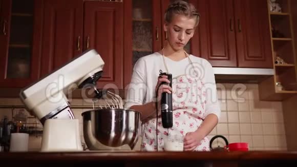 在家准备用搅拌器在厨房里鞭打奶油的年轻女子视频的预览图
