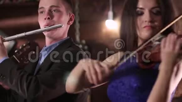 一个穿着夹克和衬衫的男人吹笛子一个穿着蓝色裙子的漂亮黑发女人拉小提琴两个人是音乐家代表视频的预览图