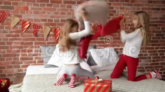 穿着睡衣的三胞姐妹用枕头安排了打斗卧室装饰着圣诞花环和圣诞节视频的预览图