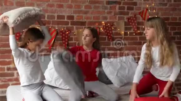 穿着圣诞睡衣的三胞姐妹正在床上打枕头仗这张床是为圣诞节装饰的梅里视频的预览图