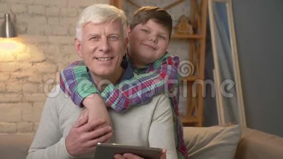 爷爷和孙子坐在沙发上看着相机微笑着一个孩子拥抱他的祖父视频的预览图