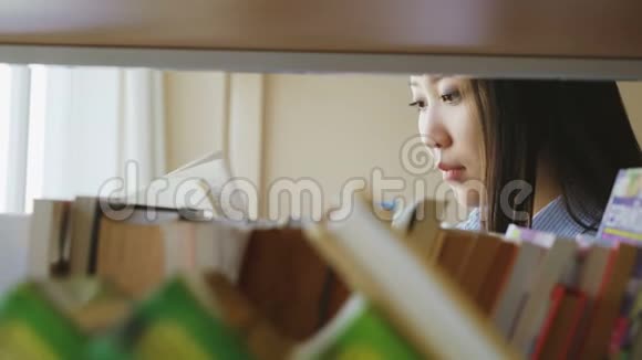 美丽的亚洲严肃的女学生站在书架旁拿着教科书的大轻图书馆里的书视频的预览图