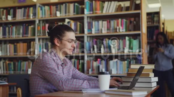 年轻英俊的时髦男学生正坐在轻巧的大图书馆里面前有一台笔记本电脑正在打印视频的预览图