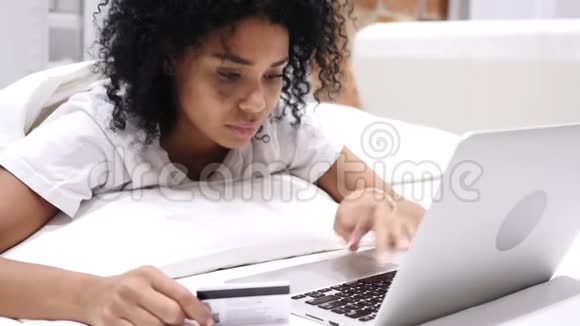 非裔美国妇女在床上网上购物用信用卡支付视频的预览图
