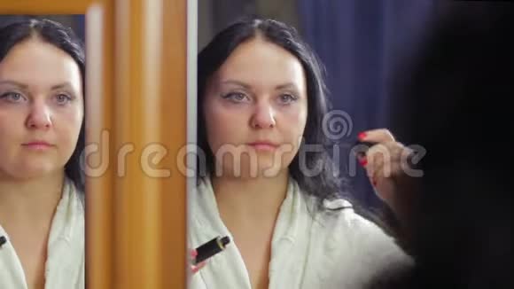 一个穿着白大褂的年轻女子在镜子前用睫毛膏涂睫毛视频的预览图